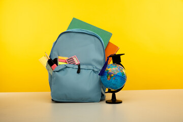 Blue backpack with school supplies with globe on yellow background