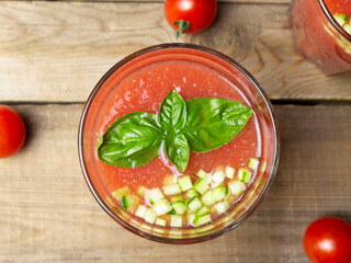 Top view of gazpacho soup in glass with basil leaves and fresh sliced brunois cucumber on wooden table