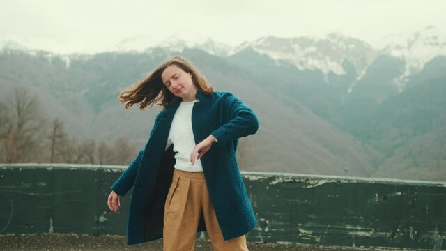 A young hipster girl dancing overlooking a big snowy mountain.