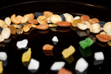 various varieties of nuts and candied fruit in a black shiny plate are reflected