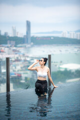 Asian travel concept. young woman enjoying with the city sky view from hotel roof top swimming pool, beautiful girl lifestyle outdoor in vacation time