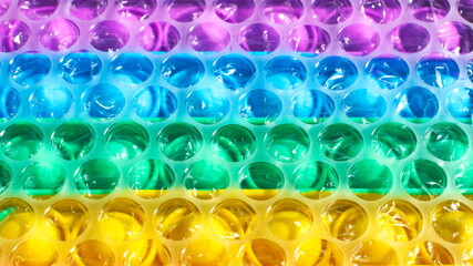 Bubble wrap film over a rainbow Pop It fidget toy. Close-up