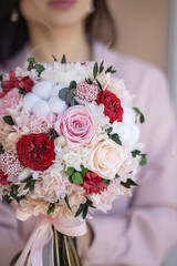 Classical bridal bouquet of preserved red rose and cotton flowers in hands. Bridal bouquet. Wedding bouquet of preserved flowers and cotton.