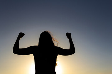 Backlit silhouette of a woman in a position of overcoming, strength and power. Sunset. Strong...