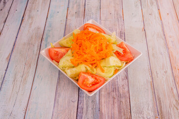 Salad with tomato, peeled and chopped cucumbers, iceberg lettuce and lots of grated carrots on a square white bowl