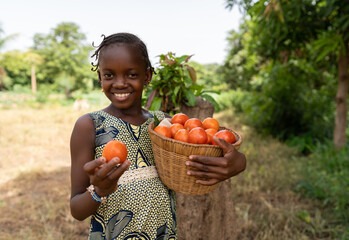 Adorable small black African girl with a straw basket full of ripe tomatoes