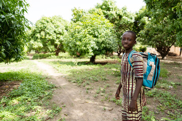 Happy little african schoolboy on his way to school walking on a small dirt path in the middle of a mango forest