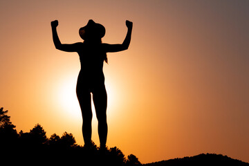 Fototapeta na wymiar Silhouette of woman at sunset, facing the sun, wearing a hat. Concept of strength and overcoming. Selective focus. Overcoming problems. Reaching a goal. Copy space. Self-confidence.