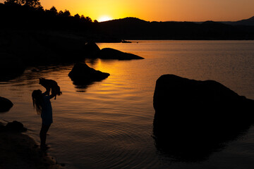 Woman on the shore of a lake at sunset with a dog caught. Love for animals.