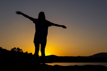 Fototapeta na wymiar Silhouette of woman at sunset with outstretched arms. Overcoming life's difficulties. Concept of reflection and thought. Selective focus. Copy space. Reaching a goal. Self-confidence.