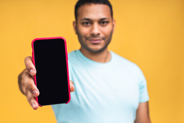 Black male african american indian man touching mobile phone display and pointing with index finger at blank screen, isolated over yellow background, copy space, cutout.