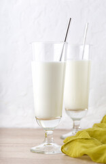 Vertical image of traditional indian milk drink in two glasses on brown wooden table with yellow cloth. Lassi made from yogurt with water, spices and ice. Ayran or kefir on white background
