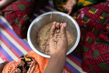 Hungry black African girl's hand taking a serving of cereals out of a metal plate shared with other...