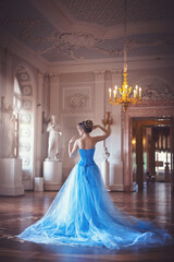 Beautiful young girl in a blue ball gown in the the historical palace interiors