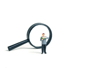 Miniature people toy figure photography. A men student standing in front of magnifier glass,...