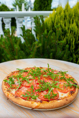 Italian pizza with herbs on a wooden table on a background with vegetation