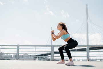 A strong female fitness trainer does strength exercises squats outdoors. Healthy lifestyle concept....