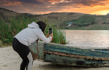 Una mujer hace una foto con su telefóno celular de un lago entre las mosntañas apoyándose en una...