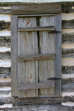 A wooden window with closed and weathered shutters on the side of a vintage woo cabin