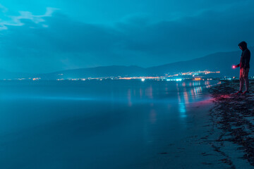 Man standing with flashlight on the beach, night scene, long exposure