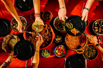 Overhead shot of a dinner table with Mexican food and hands. Tacos, beans, carnitas, habanero, salsa - Powered by Adobe