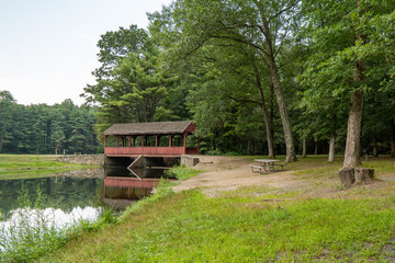 A red wooden covered bridge is surrounded by trees in the park