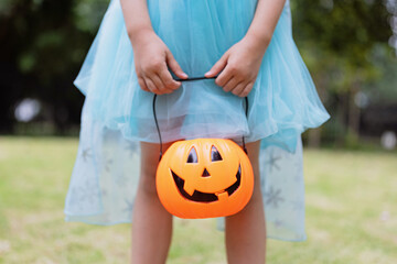 Little blonde Girl in costume of princess with Pumpkin lantern in park. Happy Halloween concept