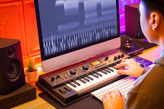 asian male professional music producer recording midi track on keyboard and desktop computer in home studio. focus on hand. music production concept