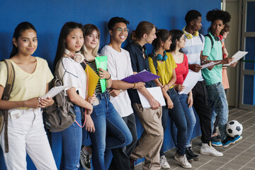 Group of multiracial teenager friends standing over blue wall. Happy Multi ethnic students in Secondary School. Focus on Center Chinese Girl