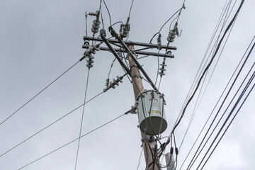 A concrete electric pole with a distribution transformer. During an overcast sky or before a storm.