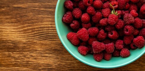 Juicy ripe bright red raspberries in a turquoise deep plate on a wooden background on the right close up