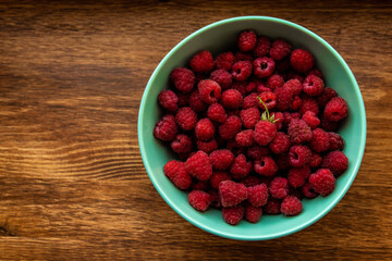 Juicy ripe bright red raspberries in a turquoise deep dish on a wooden background on the right