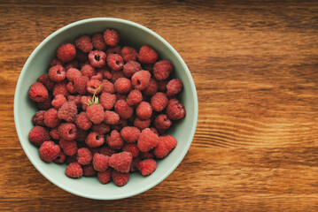 Raspberries in a turquoise deep dish on a wooden background on the left in a muted tinting