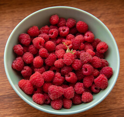 Juicy ripe bright red raspberries in a turquoise deep plate on a wooden background close-up