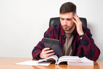 Man in amazement looks at the calculator on a light background. The calculation revealed losses. Financial audit shows losses.