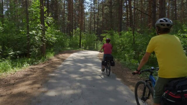 Two travelers are riding bicycles. Young men on bicycles with cycling backpacks ride along a picturesque forest road.