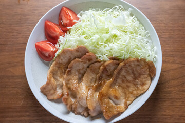 和食の中でも人気の高い、豚生姜焼きがキャベツ、トマトと共に皿に盛られている