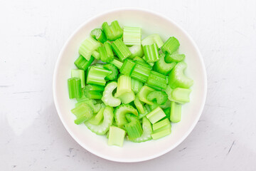 Fresh Chopped Celery Slices with Water Drops on White Dish - Top View. Vegan and Vegetarian Culture. Raw Food. Healthy Diet with Negative Calorie Content
