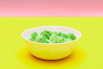 Fresh Chopped Celery Pieces with Water Drops in White Bowl on Yellow Background. Vegan and Vegetarian Culture. Raw Food. Healthy Diet with Negative Calorie Content