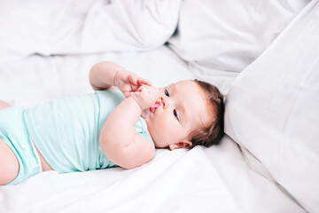 a newborn baby with a pacifier in his hands is lying on a snow-white bed