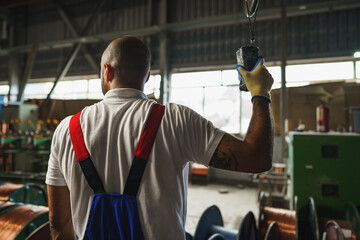 Engineer in uniform using crane controller hanging from ceiling in a factory