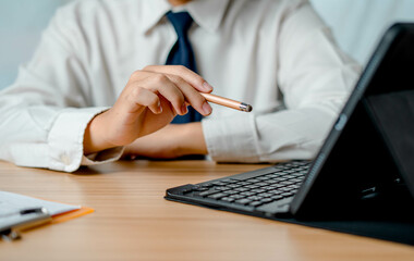 Businessman use a tablet on his desk at home busy working and connects to meeting organization. reads messages and uses a pen to write on paper. conference communication digital device long distance.