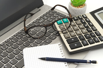 Office workstation with laptop, eyeglasses, notepad, calculator