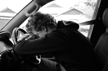 Sad and depressed mature adult man sitting in a car leaning on vehicle steering wheel