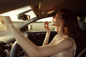 Fototapeta na wymiar Beautiful young caucasian woman painting lips on the front seat of her car