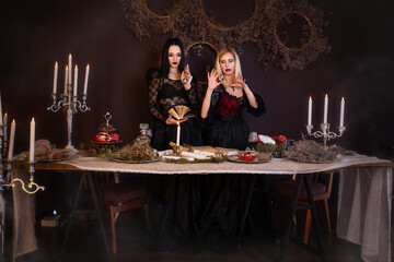Magic, fairy tale, witchcraft. Two young beautiful witches perform a magic ritual by candlelight. Two girls in beautiful black dresses. Halloween