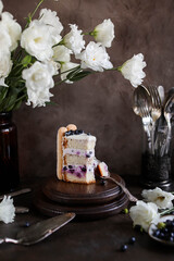 Fototapeta premium Sponge cake with blueberries and curd cream, decorated with savoyardi cookies. Beautiful cake with berries on a table with white flowers.