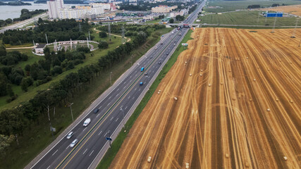 Agricultural machinery on the field. Grain harvesting. Straw bales are lying on the field. There is a busy freeway near the field. Aerial photography.