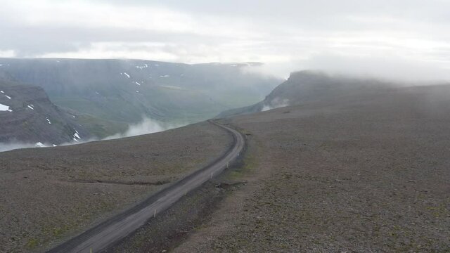 Feathery Clouds Under The Asphalt Road Amidst The Rough Landscape In Westfjords, Iceland. aerial