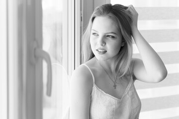 a gentle, romantic young woman in a white dress look out the window, monochrome